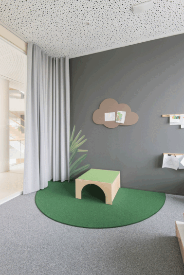 Spielecke im Eltern-Kind-Büro mit drei vielseitigen Spielpodesten, Teppich, Bilderleisten und farbenfrohem Wandgemälde – Papoq schafft kreative Räume für Familie und Arbeit.